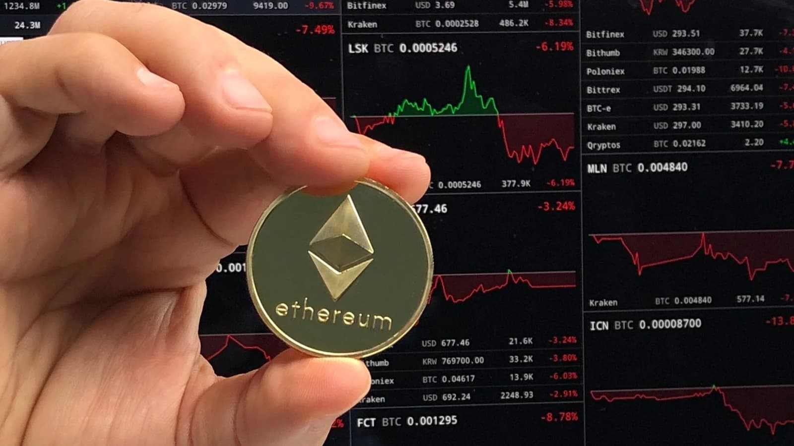 Hand holding an Ethereum coin in front of trading charts