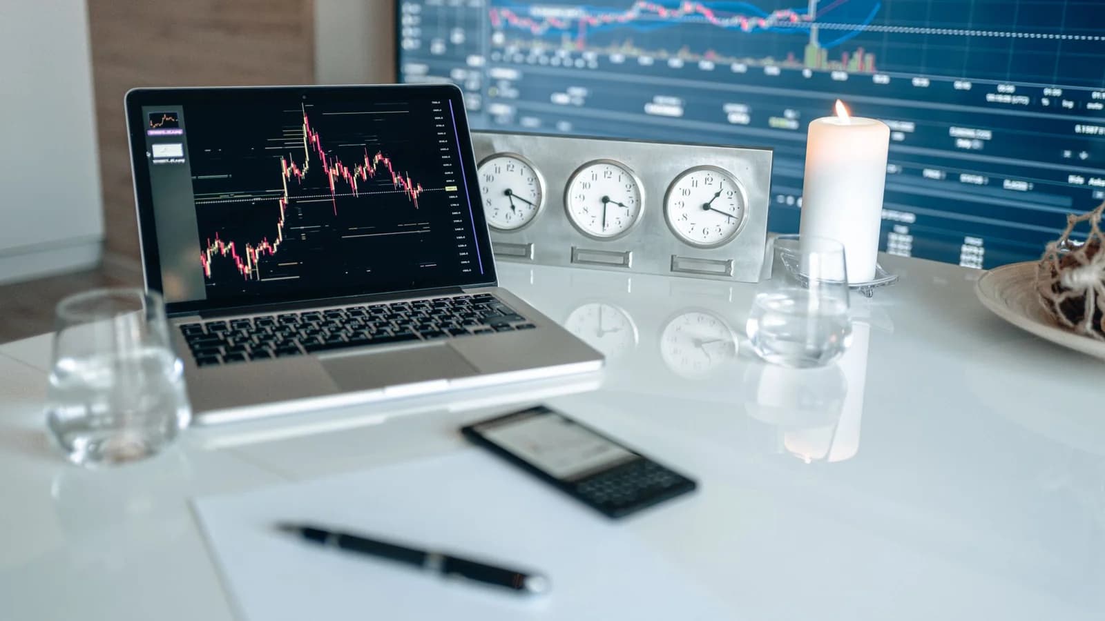 A modern workspace featuring financial charts and multiple clocks on a white table, ideal for trading.