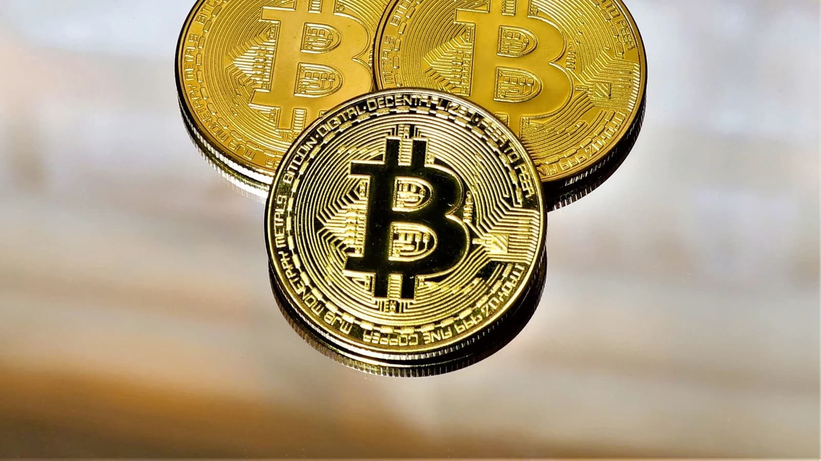Three gold Bitcoin coins on a reflective surface